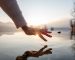 Detail of hand touching and caressing water surface of beautiful lake at sunset, mountain view. Purity freshness clean concept, one person touching lake with hand